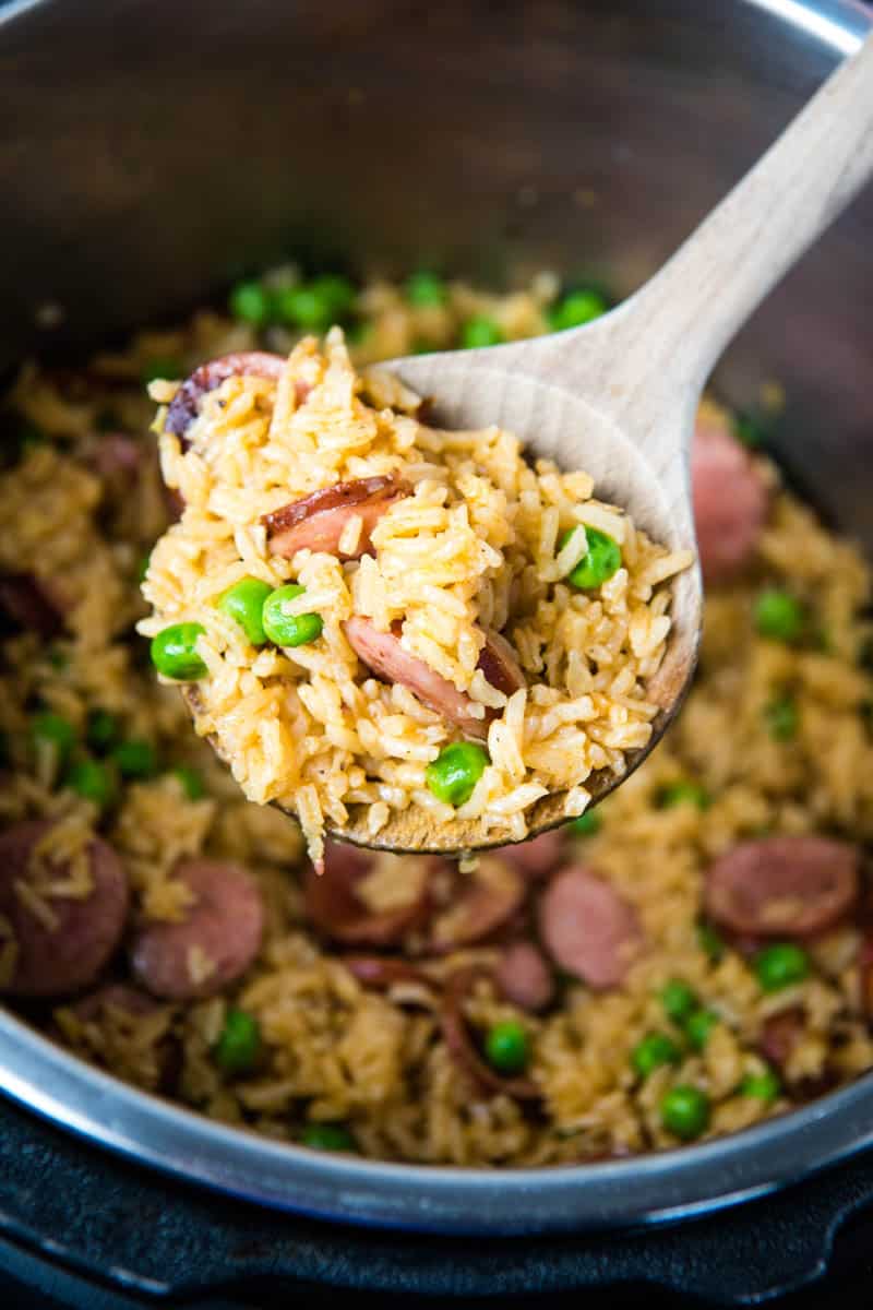 wooden spoonful of Instant Pot smoked sausage and rice with green peas over pressure cooker full of rice