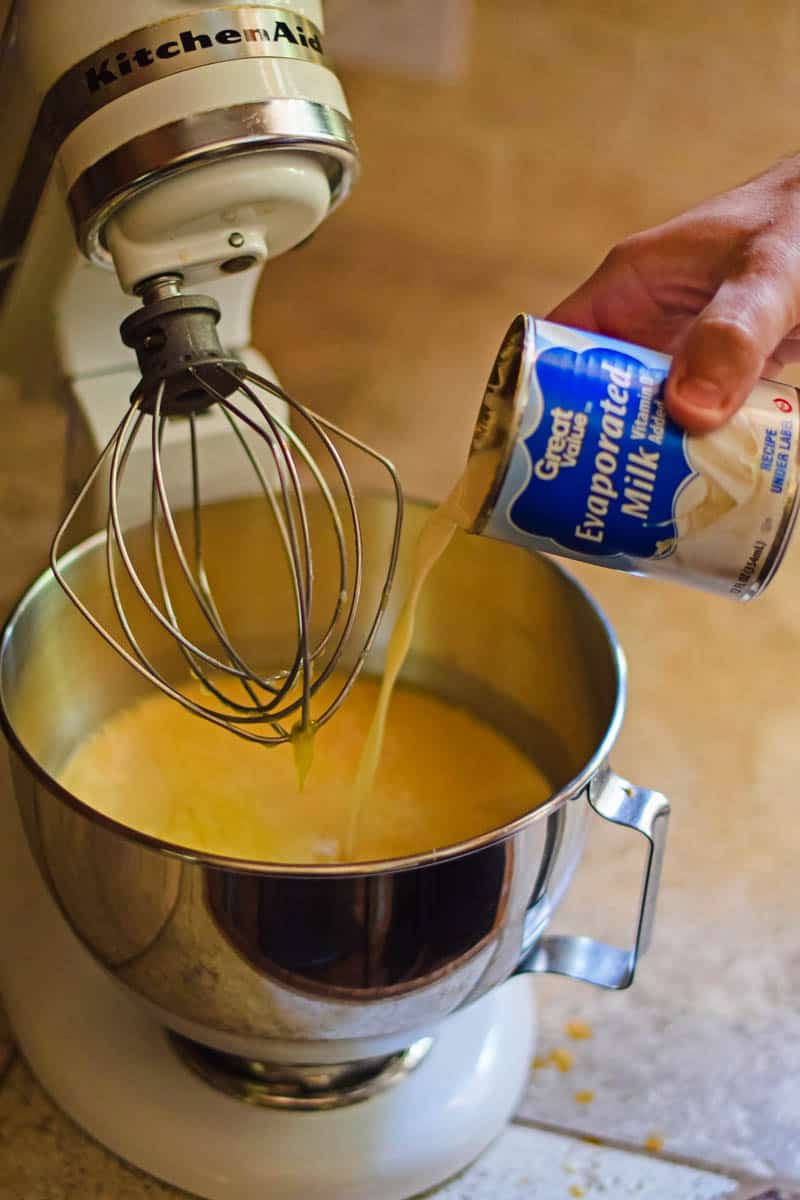 hand pouring Great Value evaporated milk into metal bowl of KitchenAid mixer full of ice cream mixture