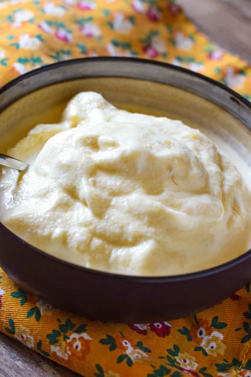 brown bowl of homemade ice cream made with bananas, with spoon, sitting on golden flower print kitchen towel