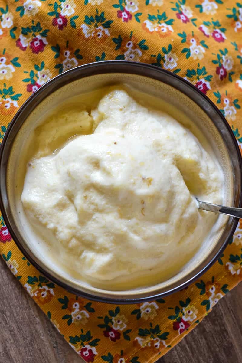 brown bowl full of old-fashioned banana ice cream with a spoon, sitting on golden flower print dish towel