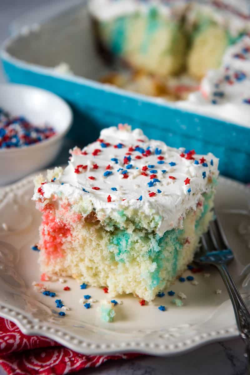 slice of red white and blue patriotic poke cake on white plate with fork