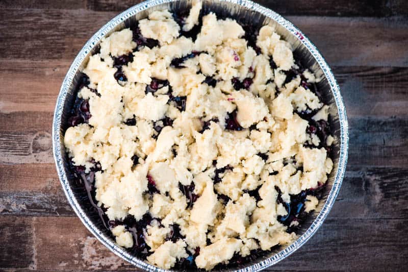 sugar cookie topping crumbled over blueberry pie filling in round foil pan