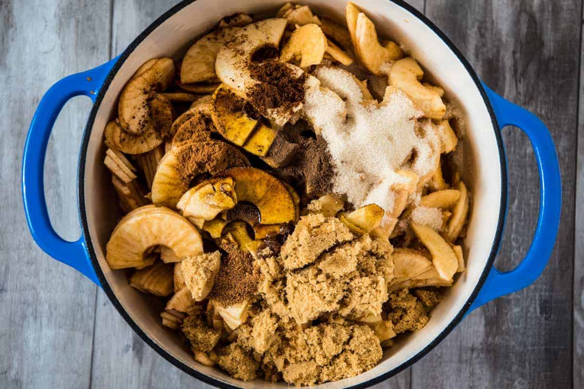 adding molasses, cinnamon, sugar, brown sugar, and spices to sliced apples in blue Dutch oven