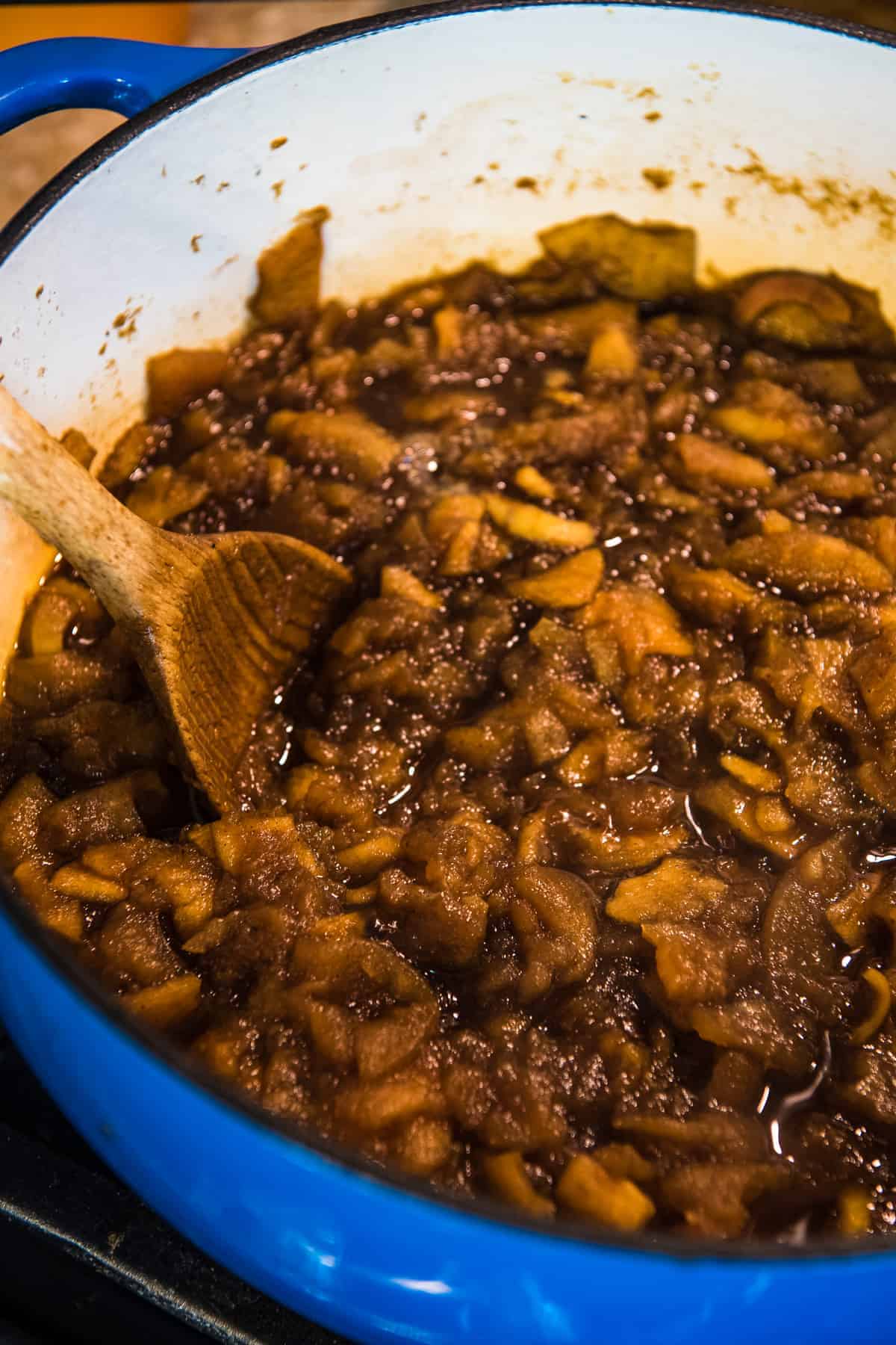 cooking traditional apple butter recipe in blue Dutch oven with wooden spoon