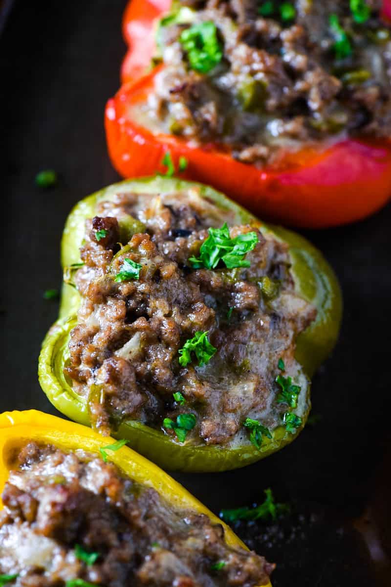 Philly cheesesteak stuffed bell peppers, including green stuffed pepper, on baking sheet