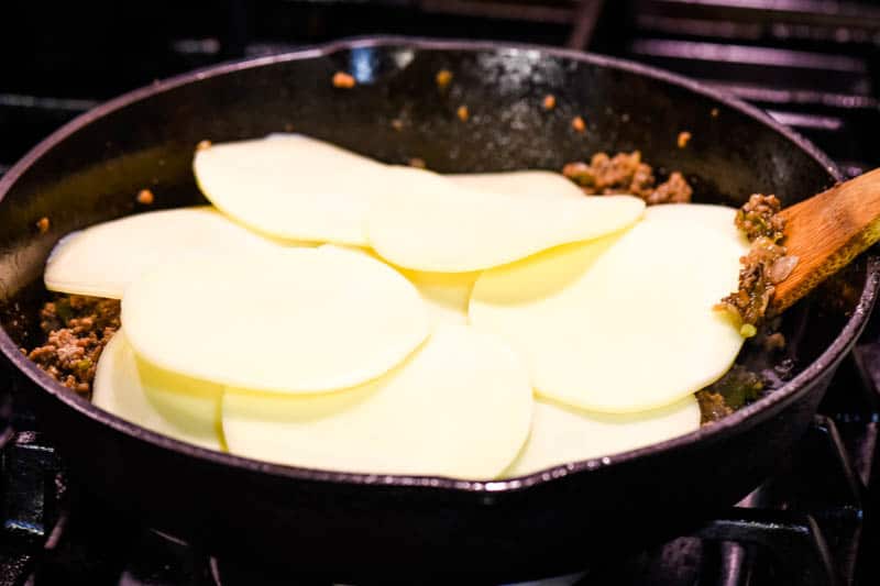 provolone cheese on cheesesteak ground beef mixture in cast iron skillet with wooden spatula