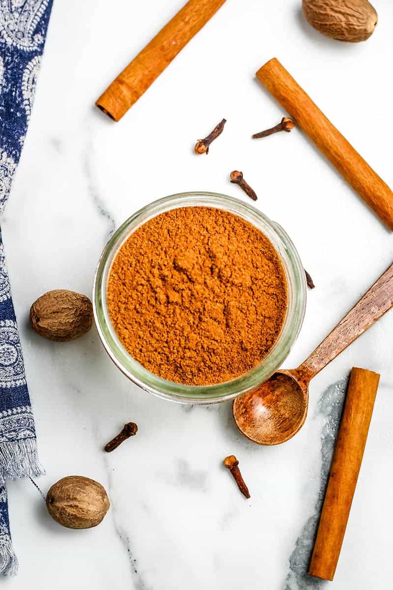 homemade pumpkin spice blend in small mason jar on white marble countertop with cinnamon sticks and small wooden spoon