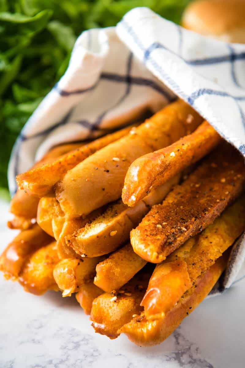 stack of quick and easy breadsticks from hot dog buns in white and blue striped towel on white marble countertop