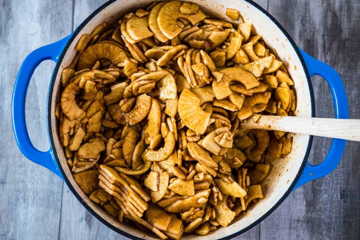 stirring apple butter ingredients in blue Dutch oven with wooden spoon