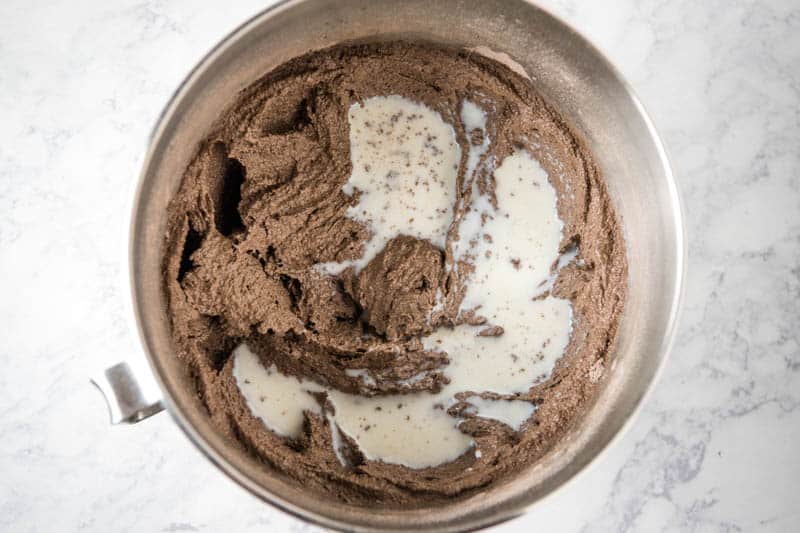 adding buttermilk to chocolate cupcake batter in KitchenAid mixing bowl on white marble countertop