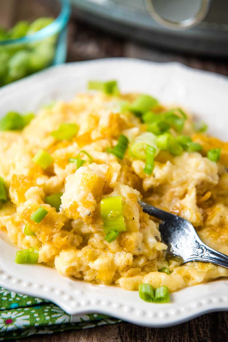 serving of CrockPot hashbrown casserole, sprinkled with green onions, on white plate with fork