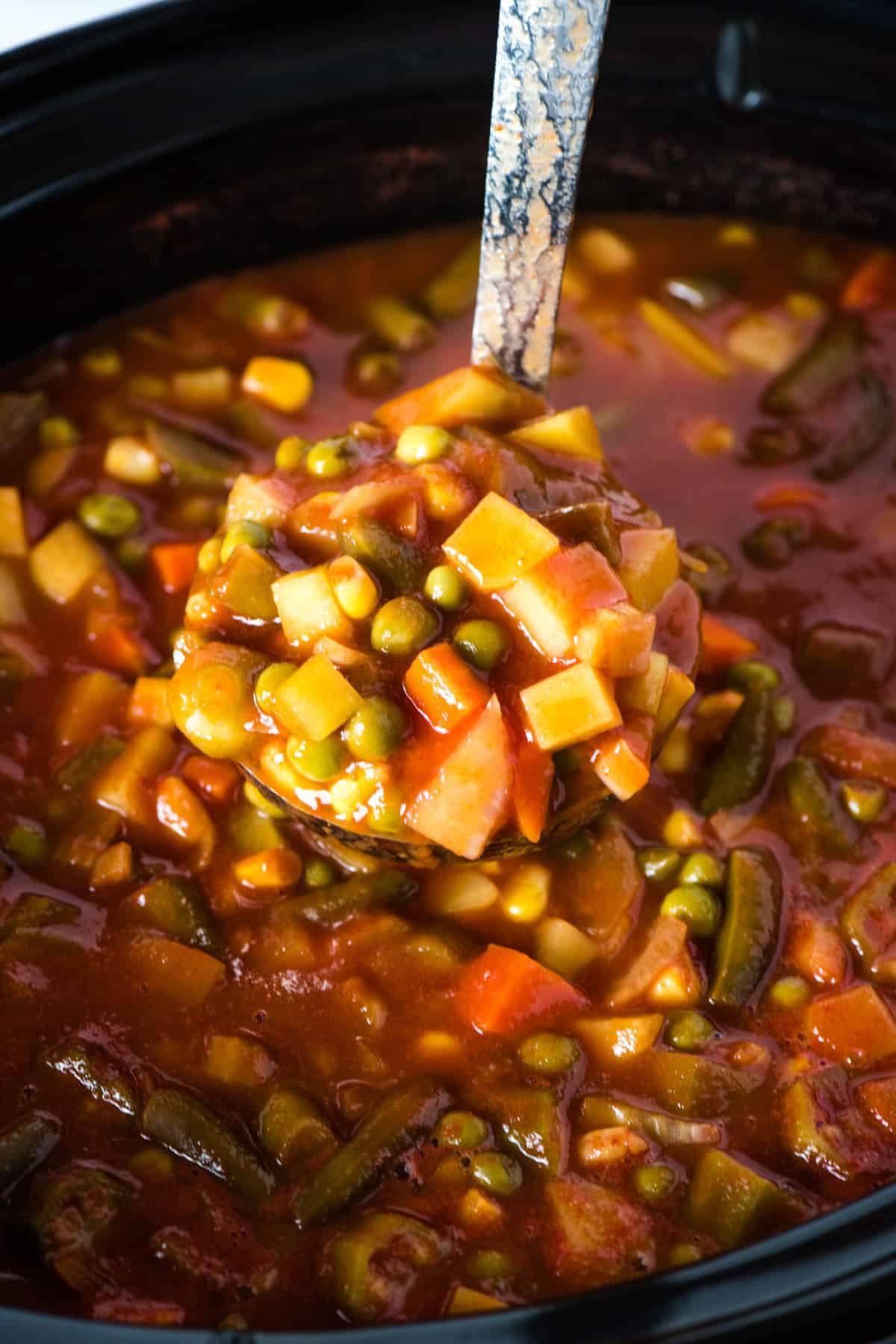 ladle full of CrockPot V8 soup over black slow cooker full of soup