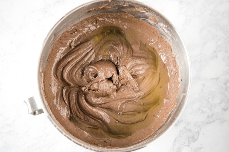 adding egg whites to chocolate cupcake batter in KitchenAid mixing bowl on white marble countertop