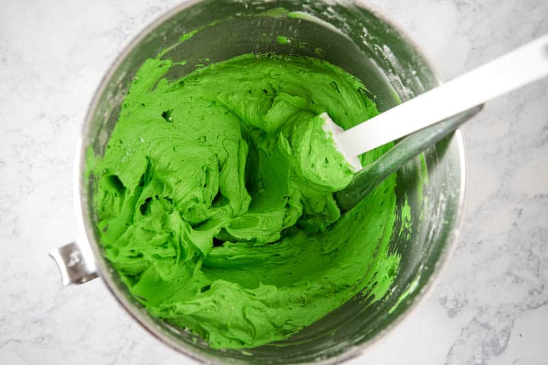 green buttercream frosting in KitchenAid mixing bowl on white marble countertop