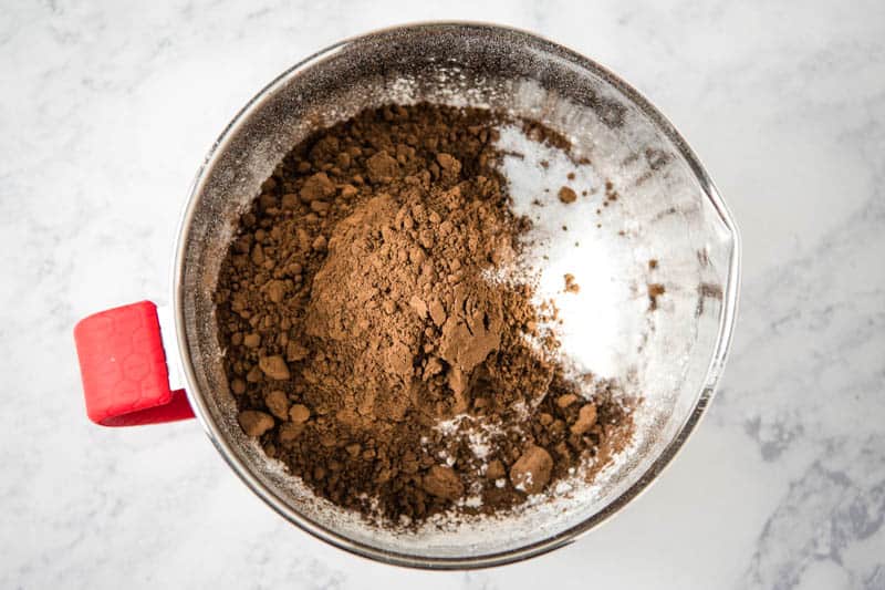 cake flour, cocoa powder, baking soda, and salt in silver mixing bowl on white marble countertop