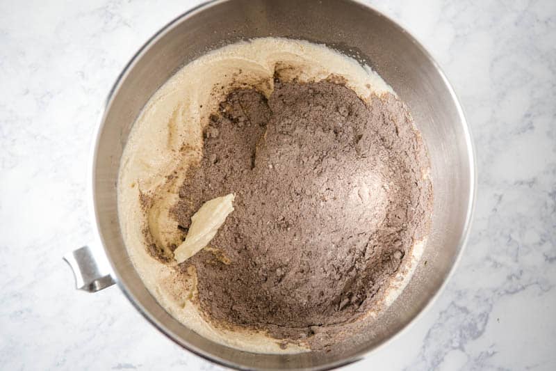 adding dry ingredients to cupcake batter in KitchenAid mixing bowl on white marble countertop