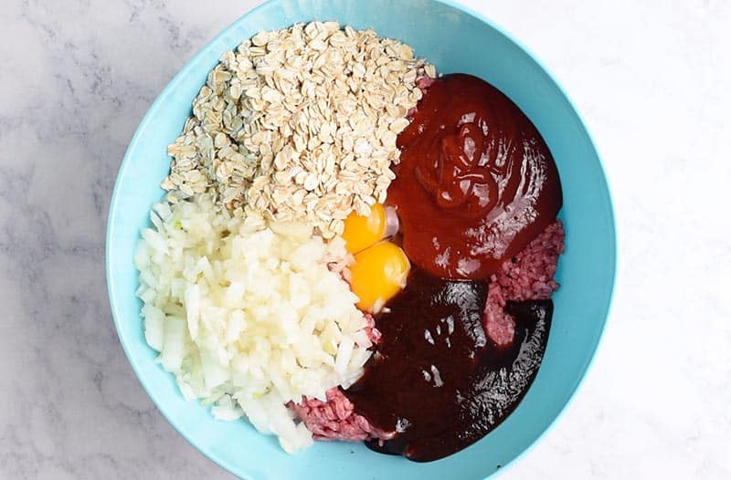 mixing ingredients for meatloaf recipe with oatmeal in blue mixing bowl