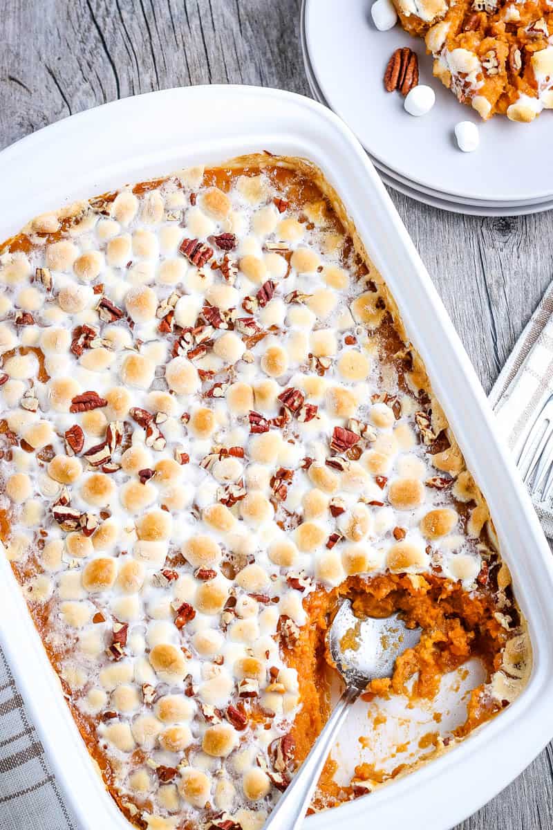 spoon scooping southern sweet potato casserole out of white baking dish and onto small white plate