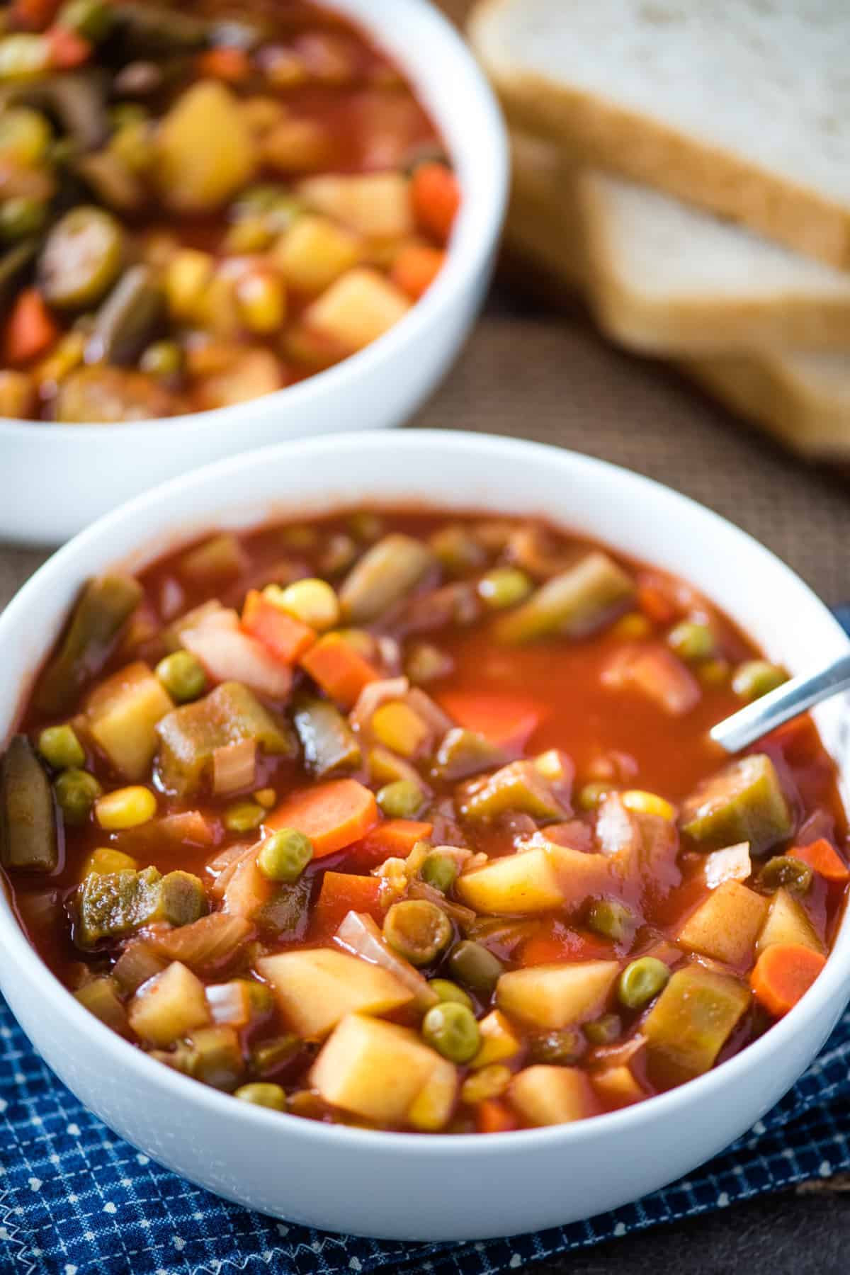white bowl of CrockPot V8 vegetable soup with spoon on blue and white checked linen