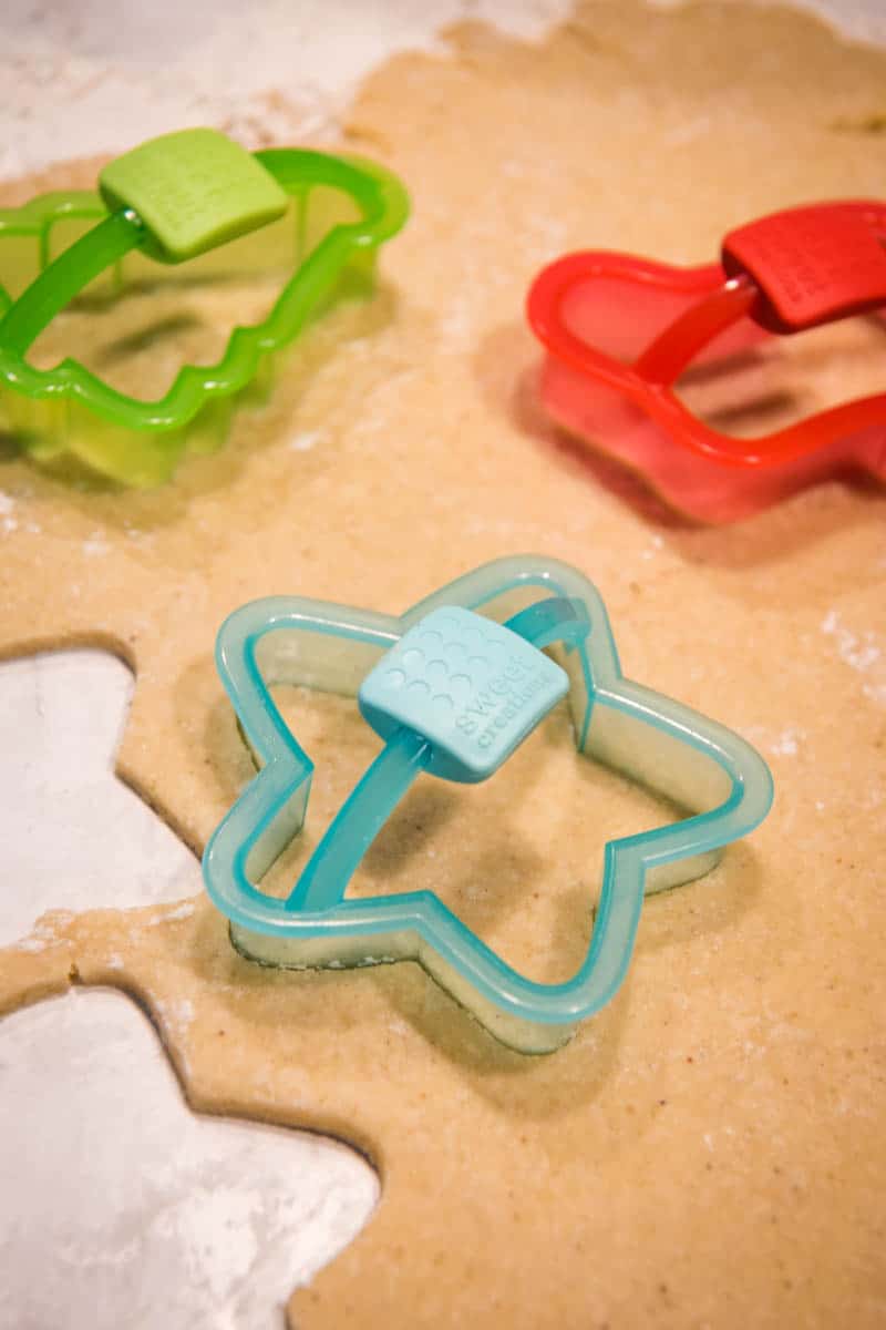Christmas cookie cutters cutting sugar cookie dough on floured surface
