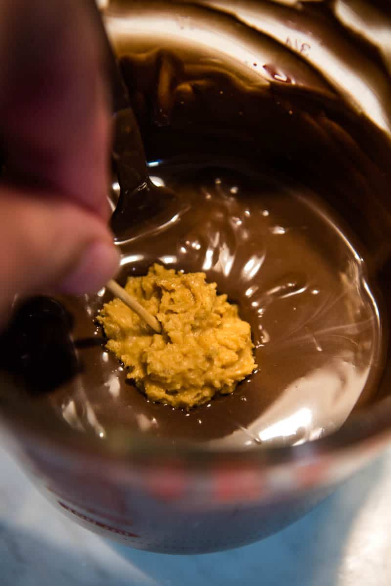 hand dipping peanut butter rice crispy balls in melted chocolate with toothpicks