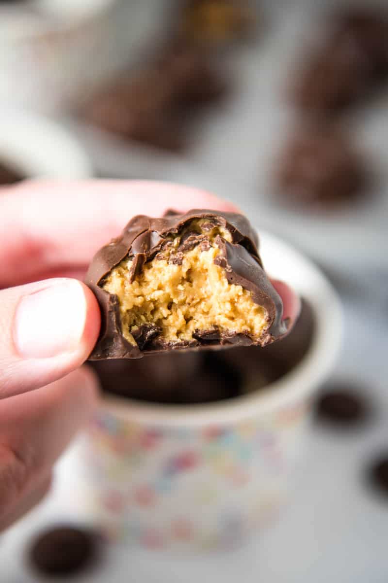 fingers holding rice crispy peanut butter ball with bite taken out