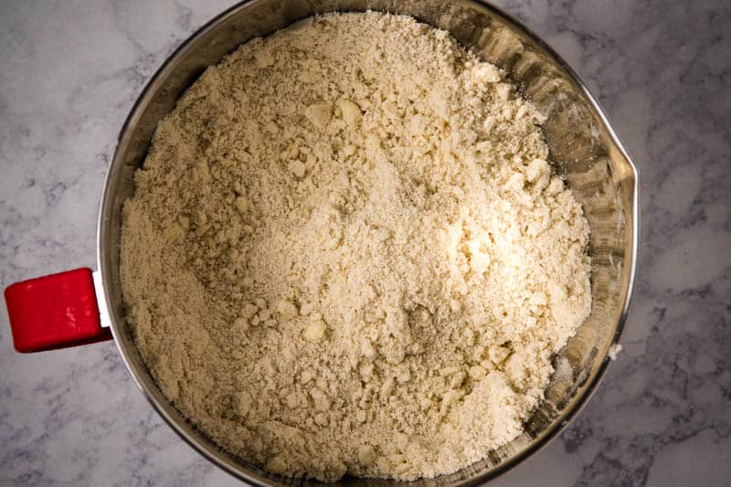 dry ingredients for sugar cookies mixed with cold butter in silver and red mixing bowl, 'til it's as fine as corn meal