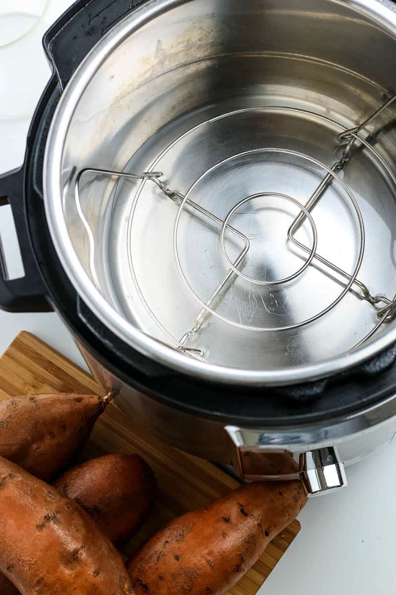 water and steaming trivet in Instant Pot with sweet potatoes on wooden cutting board