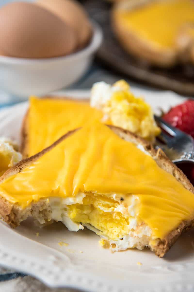 half eaten egg in a hole with cheese on white plate with fork and strawberries