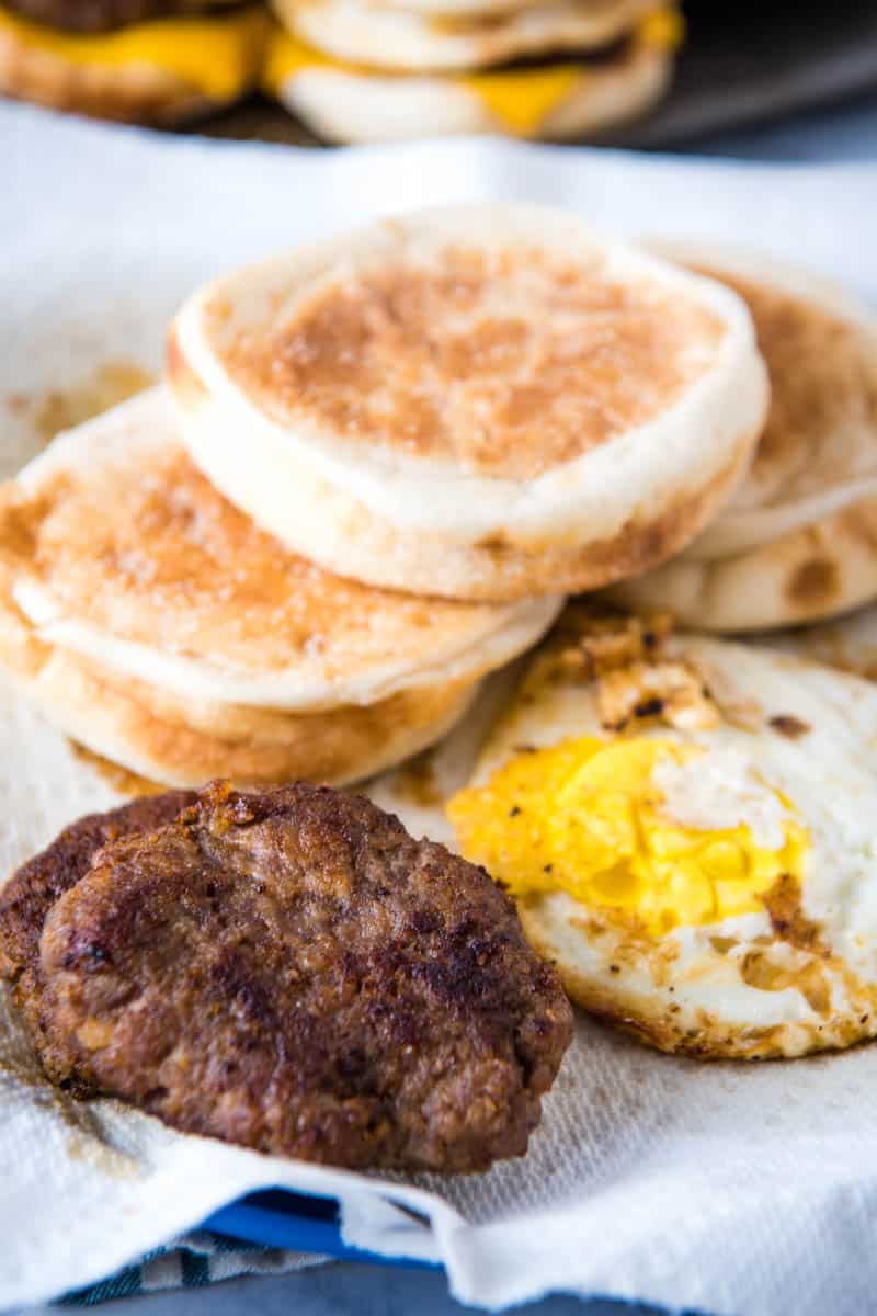 sausage McMuffin ingredients, including English muffins, sausage patties, and eggs on blue plate with paper towel