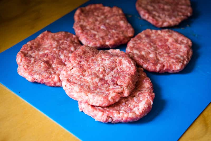 sausage patties shaped and rounded, ready for cooking, on blue cutting board
