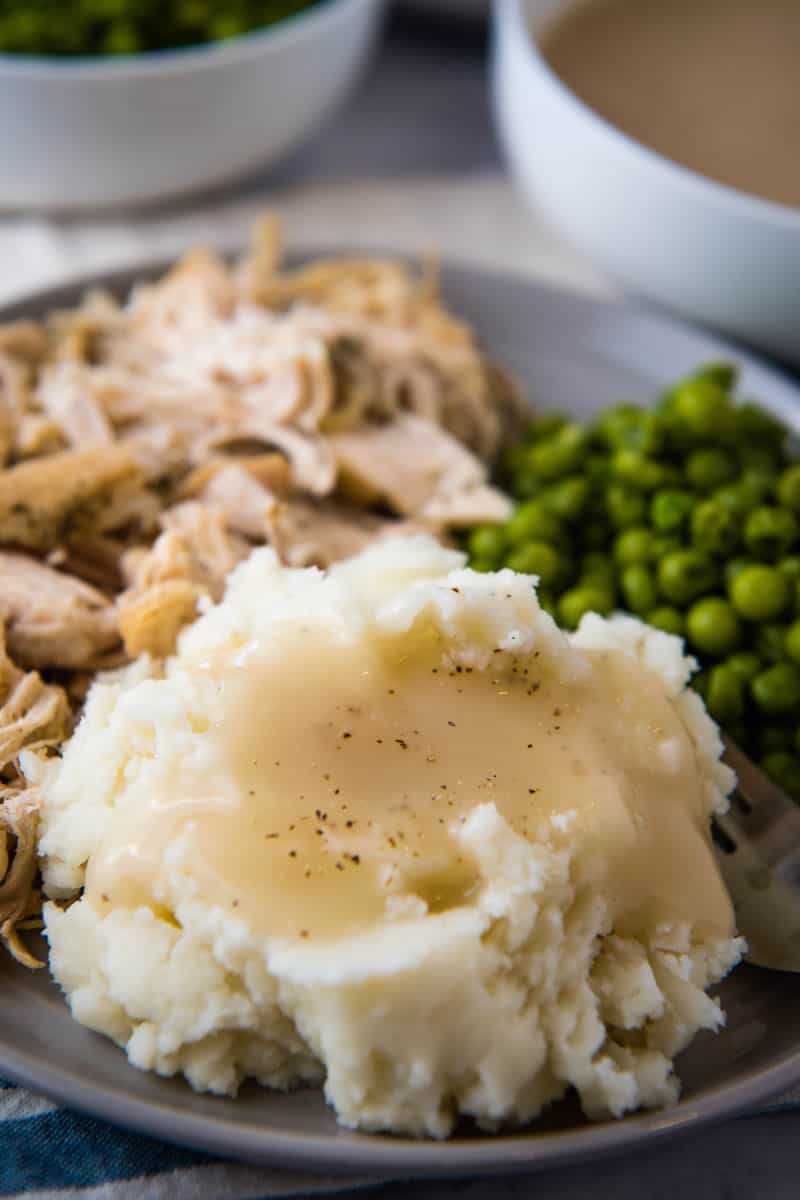 chicken gravy with bouillon poured over mashed potatoes on gray plate with shredded chicken and green peas