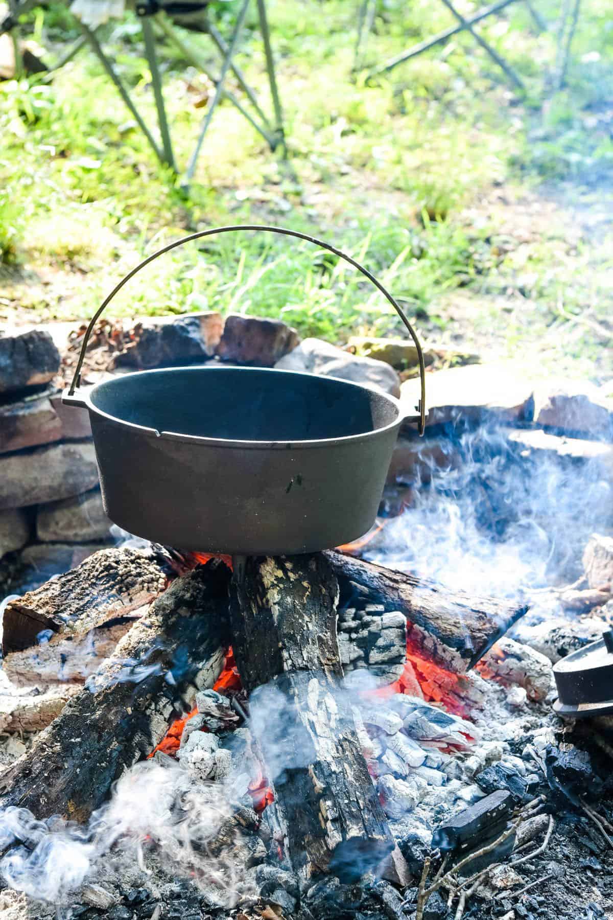 cast iron Dutch oven preheating on a bed of hot coals in the fire pit
