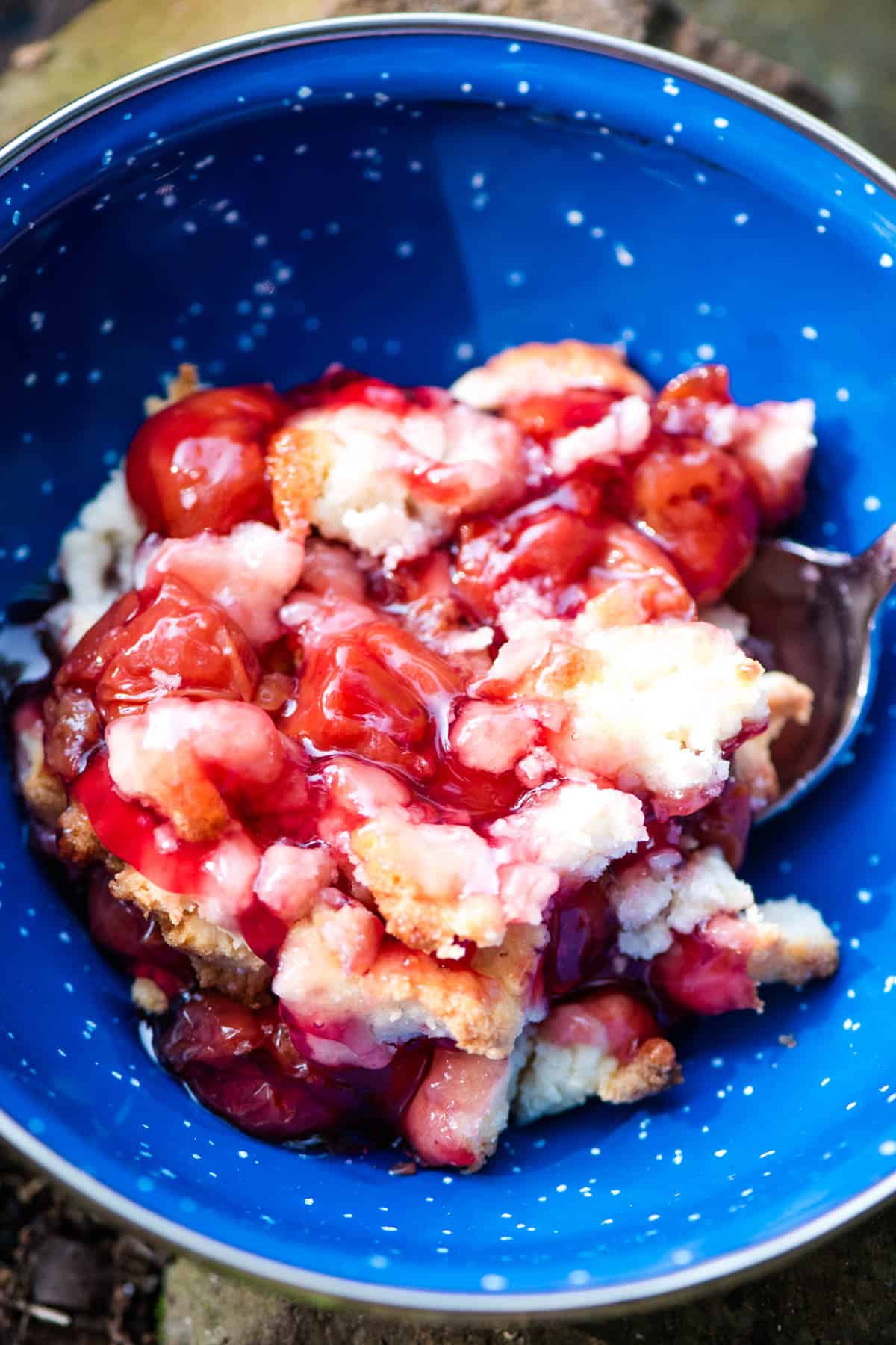 freshly baked Dutch oven cobbler served up in a small blue bowl with a small silver spoon