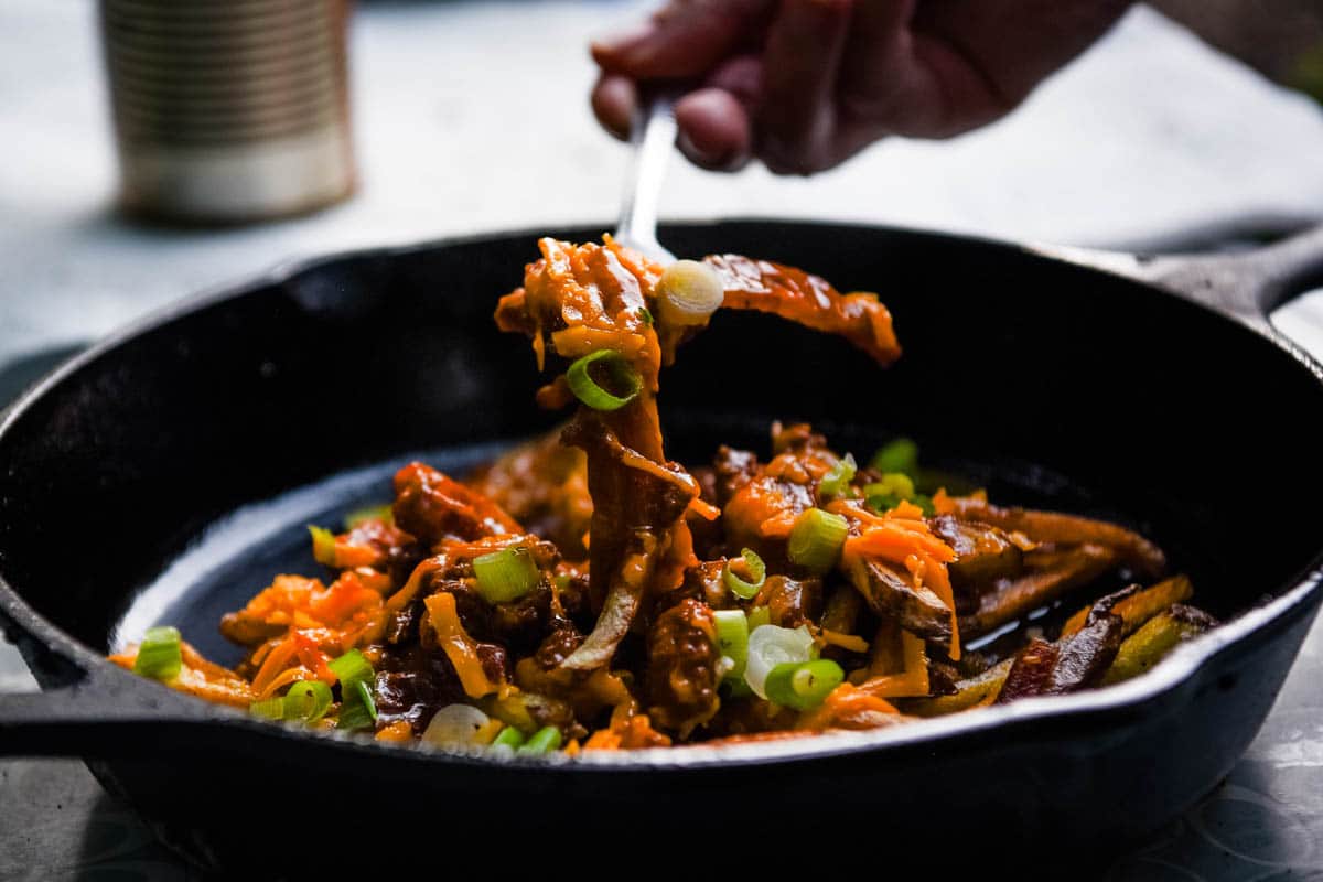 forkful of French fries with chili cheese over top of a large cast iron skillet full of chili cheese fries