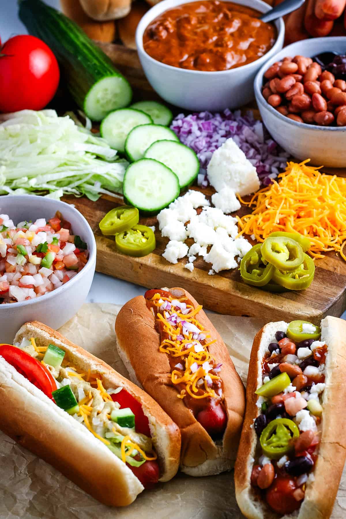 loaded Crock Pot hot dogs next to all of the toppings lined out on a large wooden cutting board