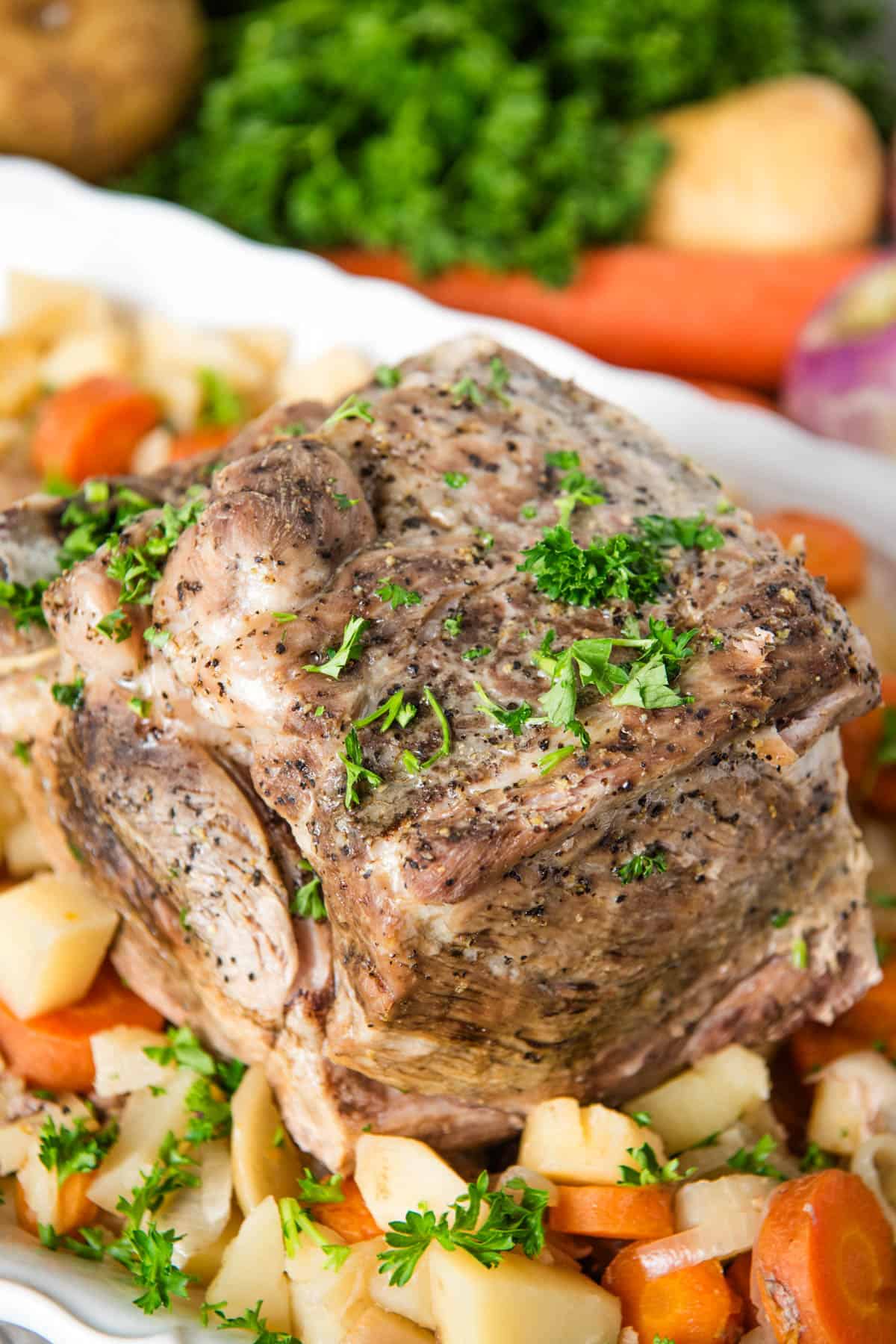 slow cooker pork roast garnished with fresh parsley on a bed of root veggies on a large white decorative plate