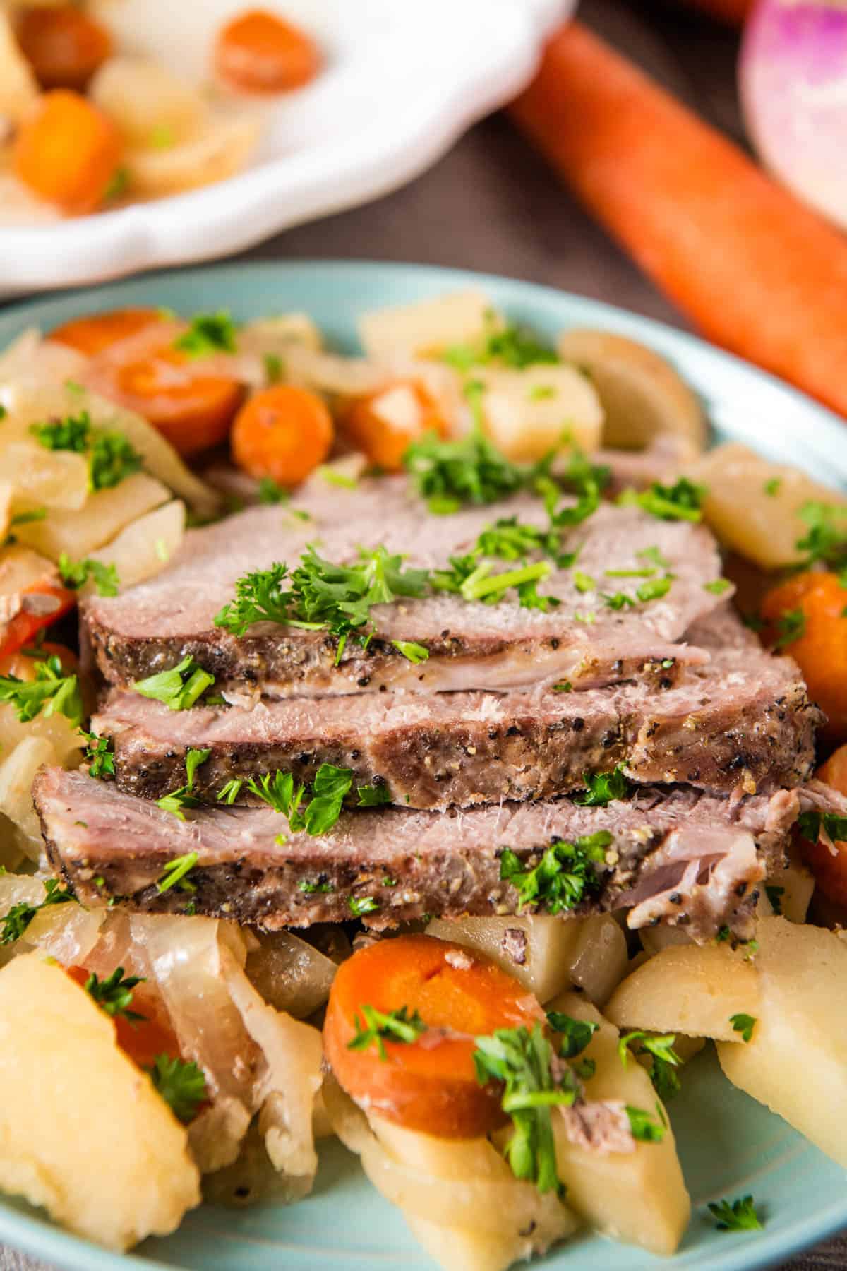 slow cooker pork roast sliced up and garnished with fresh parsley on a bed of root veggies on a small blue plate