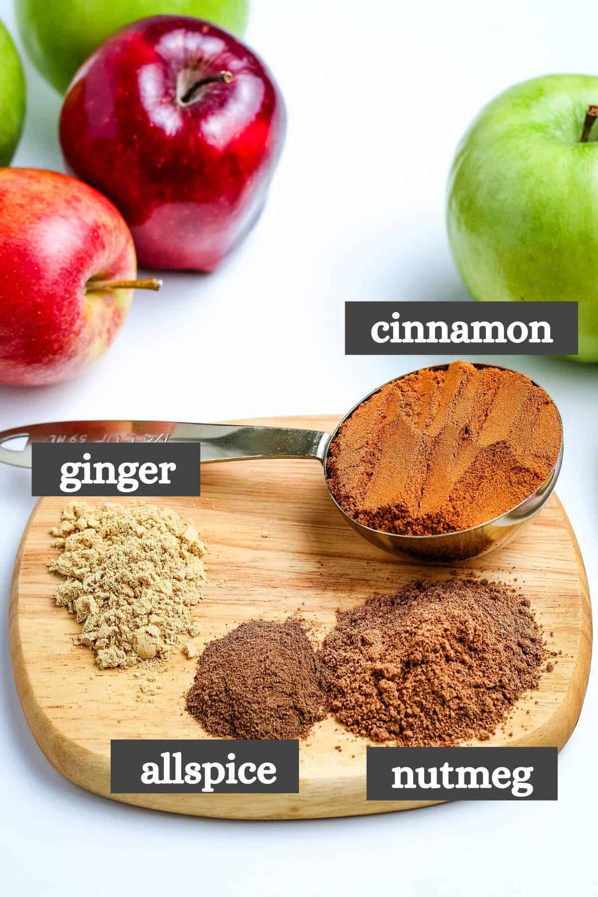 apple pie spice recipe ingredients lined out on a small wooden cutting board on a bright white countertop