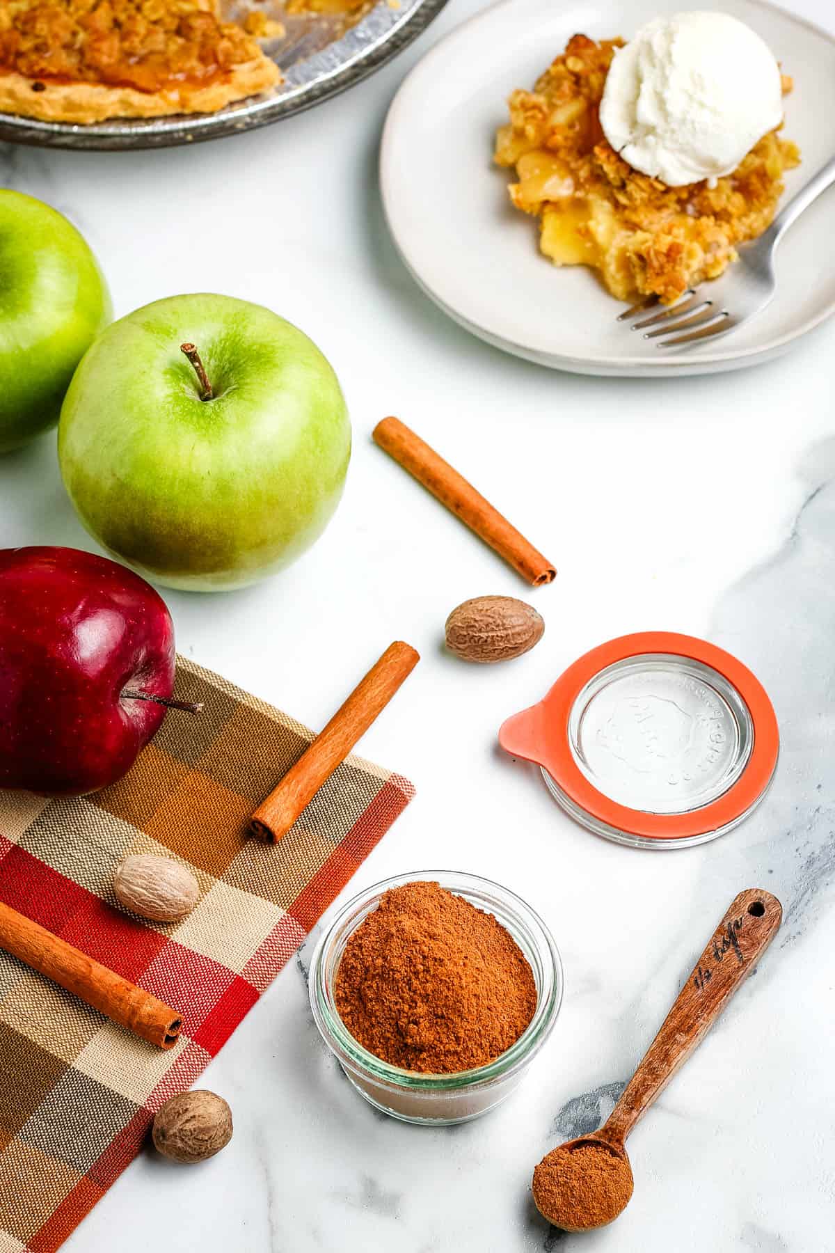 DIY apple pie spice in a small glass bowl next to a brown checkerboard cloth on a bright white countertop