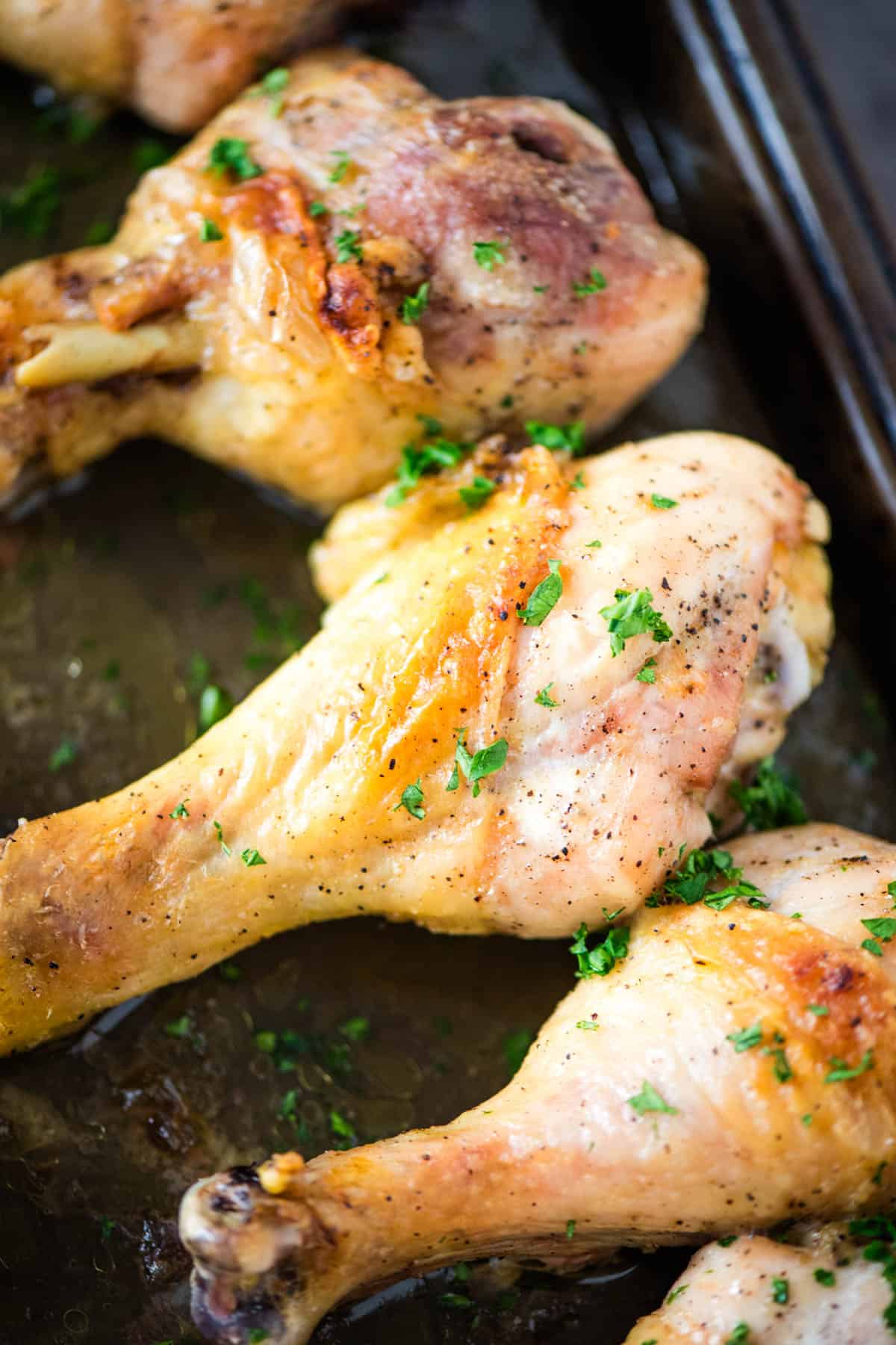 baked chicken drumsticks with a fresh parsley garnish on a large baking sheet