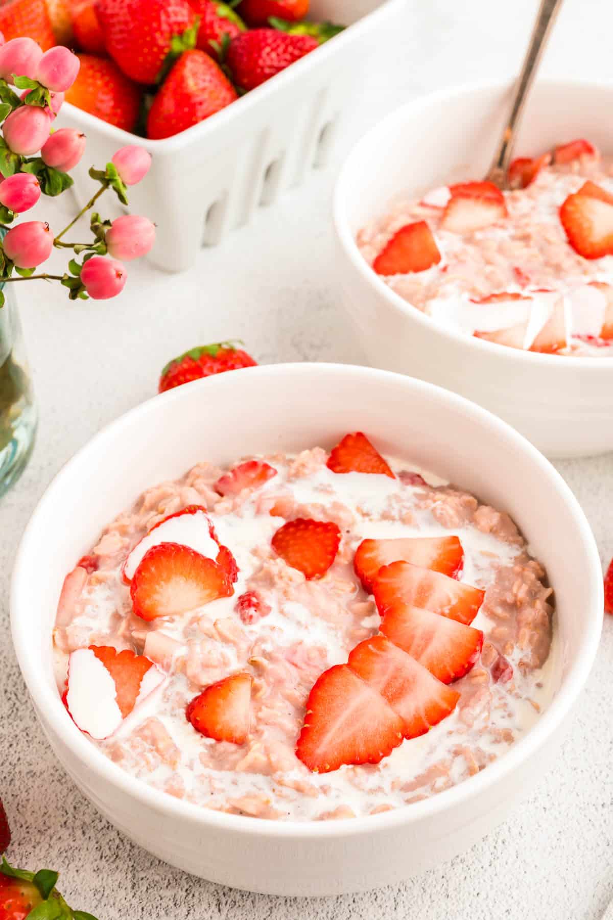 small white bowl of strawberry and cream oatmeal with heavy cream and sliced berries on top