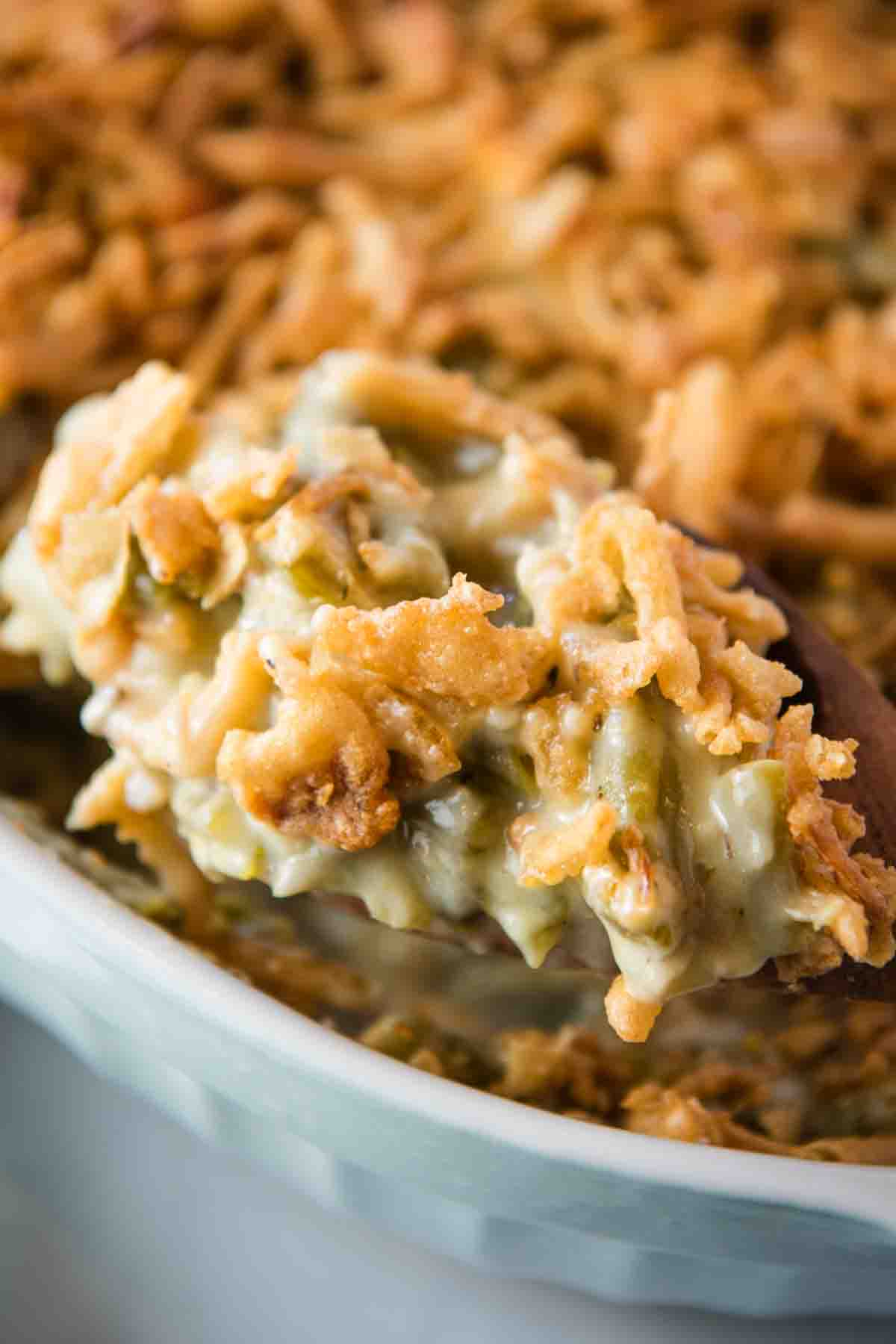 closeup photo of a heaping spoonful of green bean casserole over a white baking dish full of green bean casserole