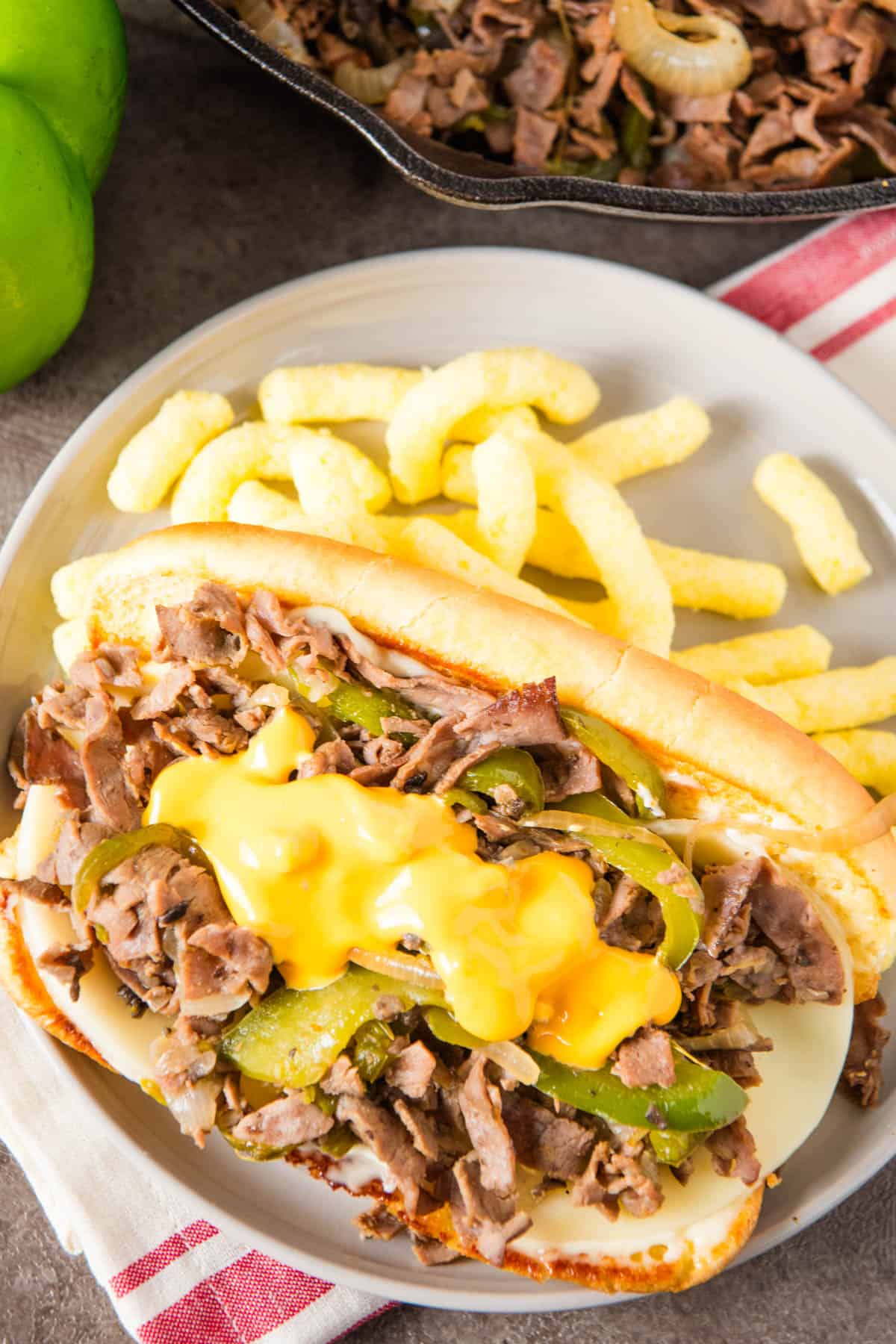 Philly cheesesteak with roast beef and Cheez Wiz on top on a small gray plate with white cheddar cheetos on the side