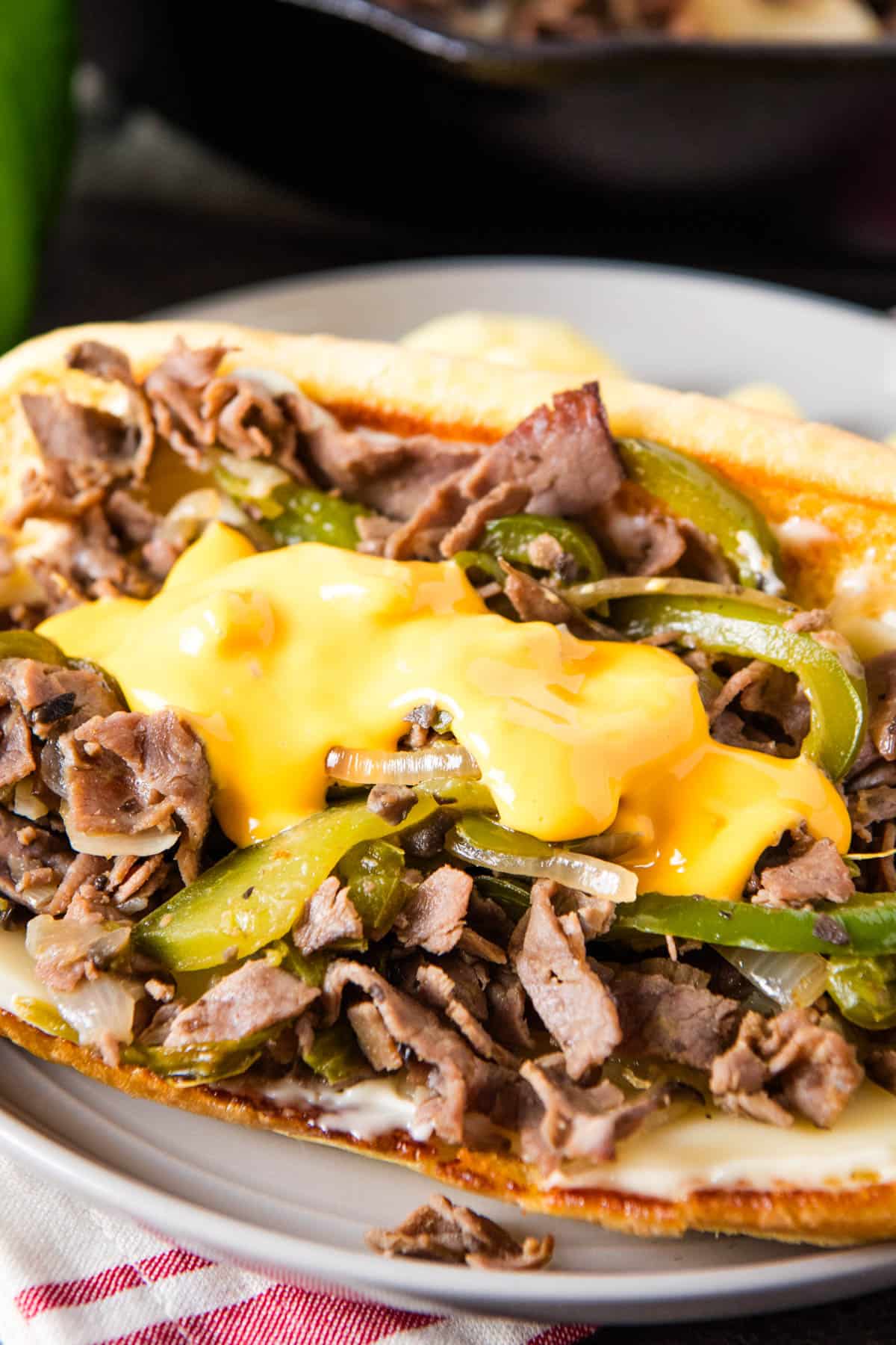 closeup photo of roast beef Philly cheesesteak in a hoagie roll with Cheez Wiz on top on a small gray plate with white cheddar Cheetos on the side