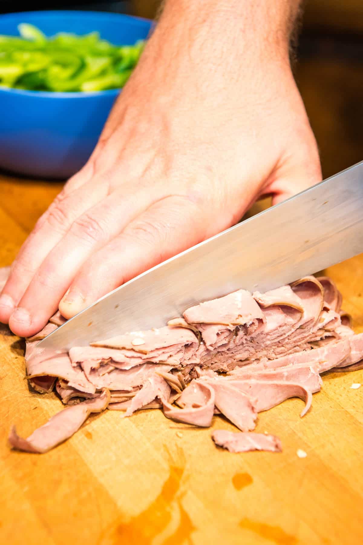 closeup photo showing slicing roast beef lunch meat with a large knife on a large brown wooden cutting board