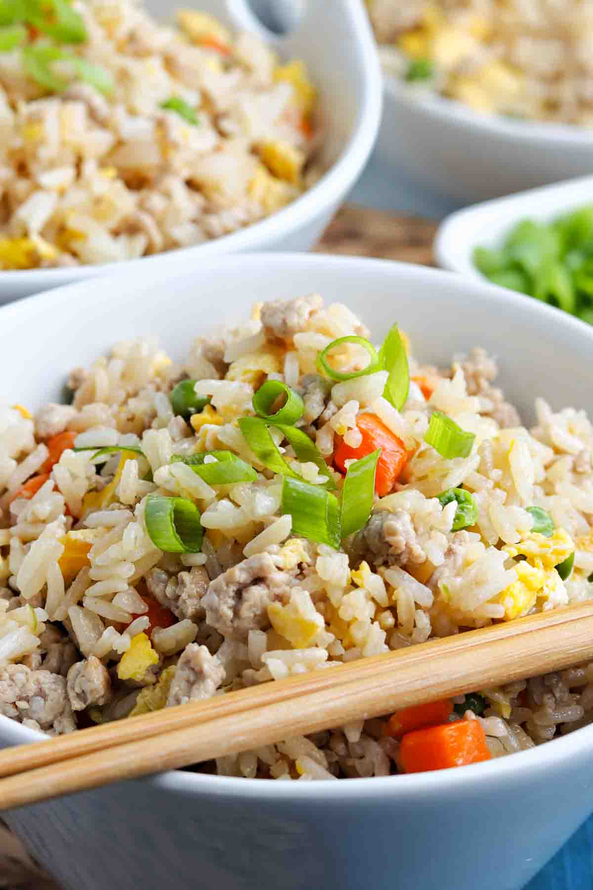 closeup photo of a small white bowl full of pork fried rice with a pair of wooden chopsticks on top of the bowl