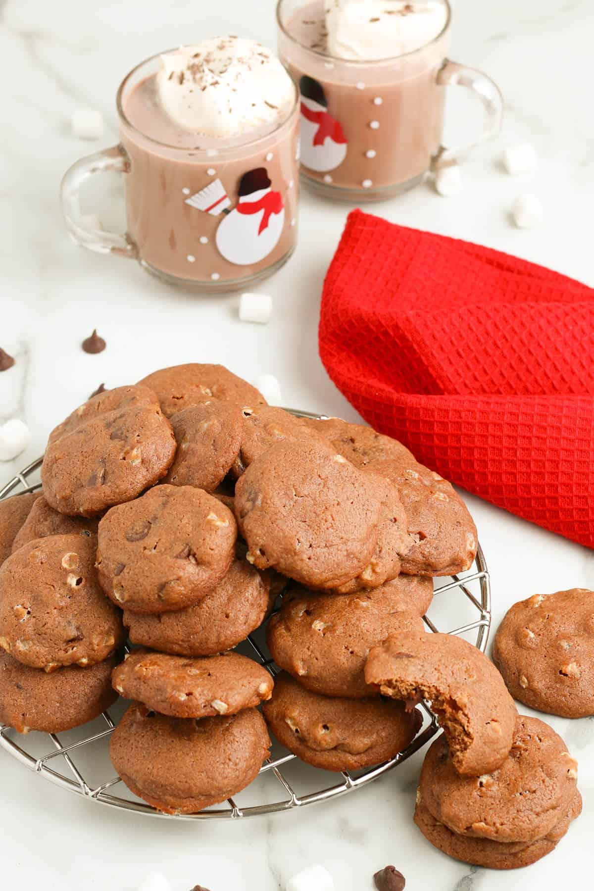 hot chocolate marshmallow cookies piled up on a silver wire cooling rack on a white countertop