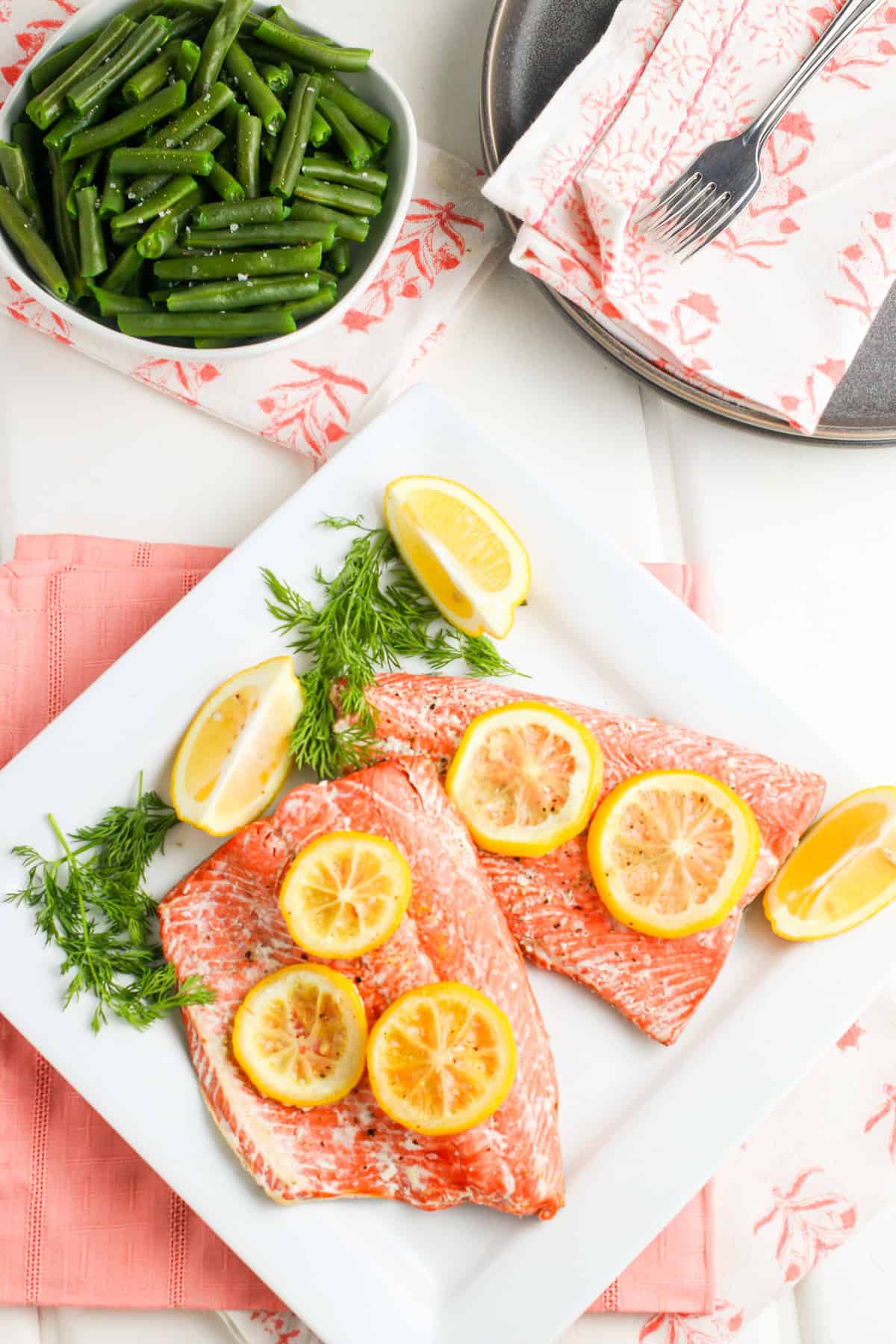 pressure cooker salmon fillets lined out on a decorative white plate with fresh lemon slices on top and fresh dill sprigs on the side