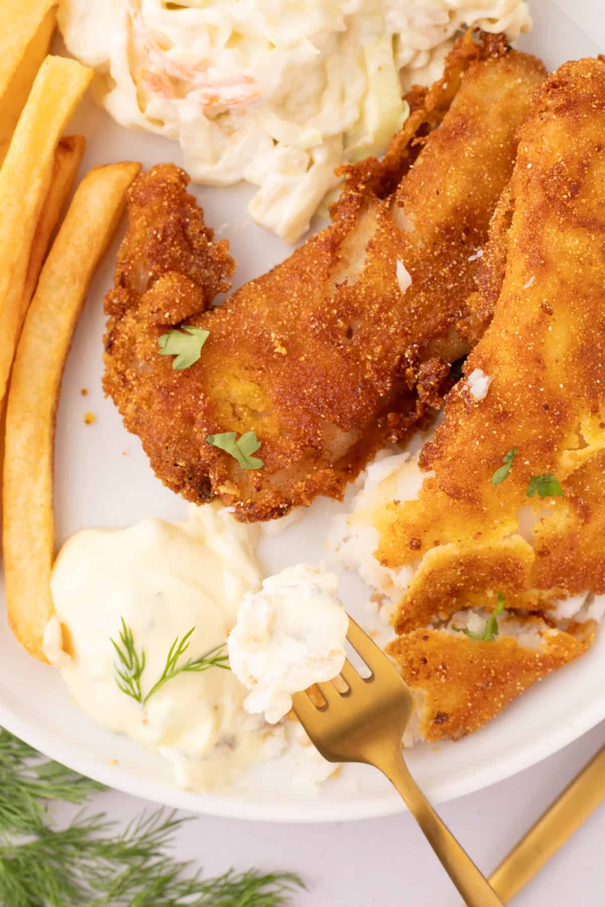 fried crappie fillets on a large white decorative plate with French fries and pasta salad on the side